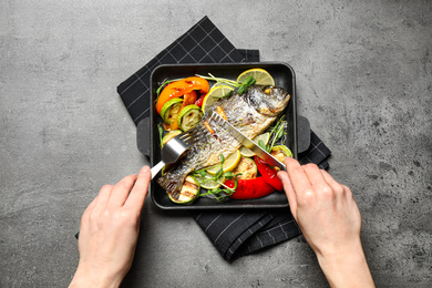 Woman eating delicious roasted fish at grey table, top view