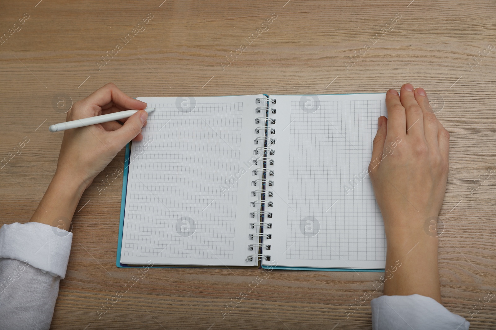 Photo of Left-handed woman writing in notebook at wooden table, above view