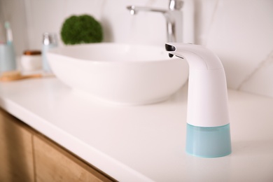 Modern automatic soap dispenser on countertop in bathroom. Space for text