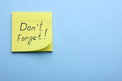 Photo of Paper note with phrase Don't Forget on light blue background, top view. Space for text