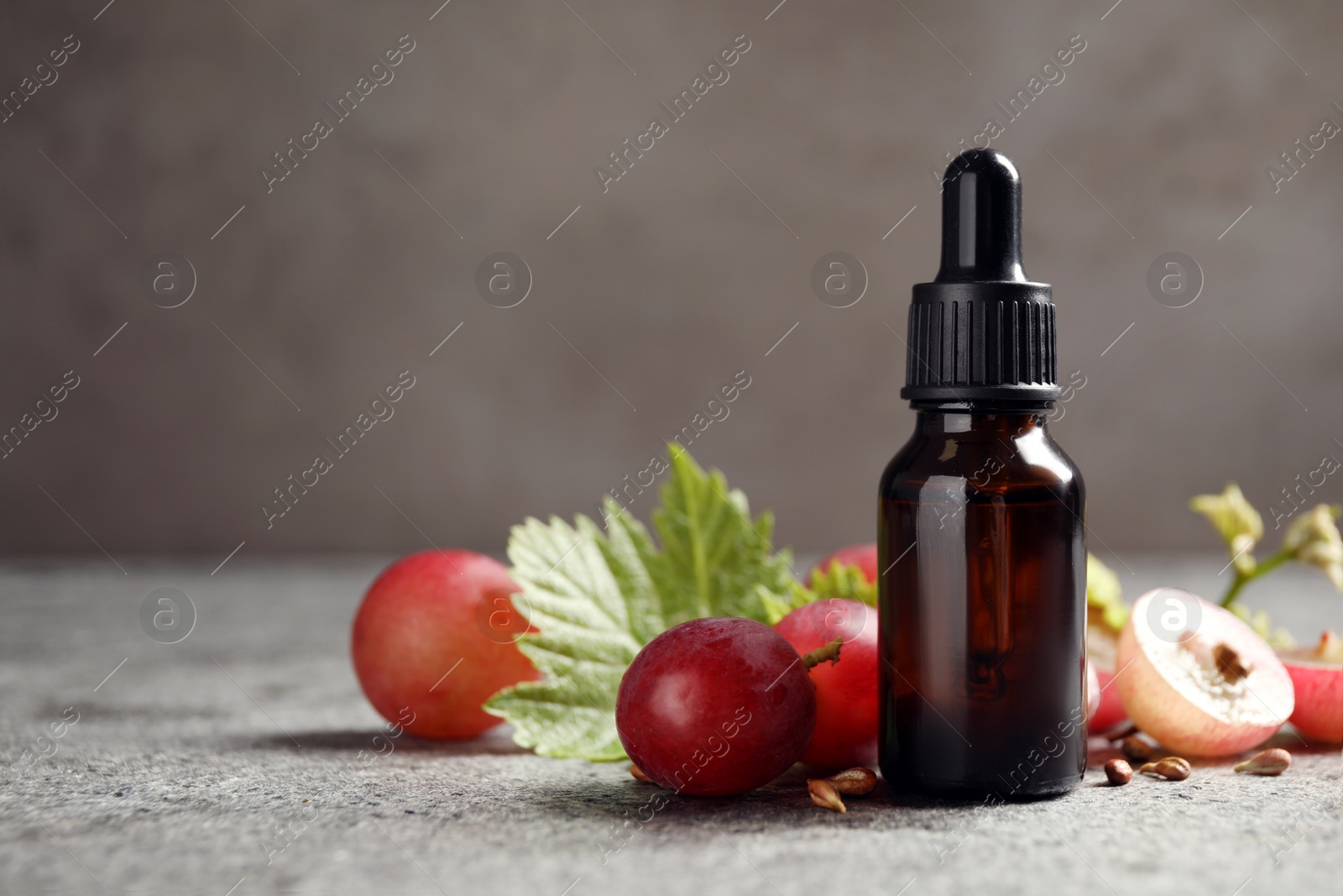 Photo of Bottle of natural grape seed oil on grey table, space for text. Organic cosmetic