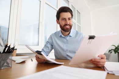 Happy businessman working with documents at wooden table in office