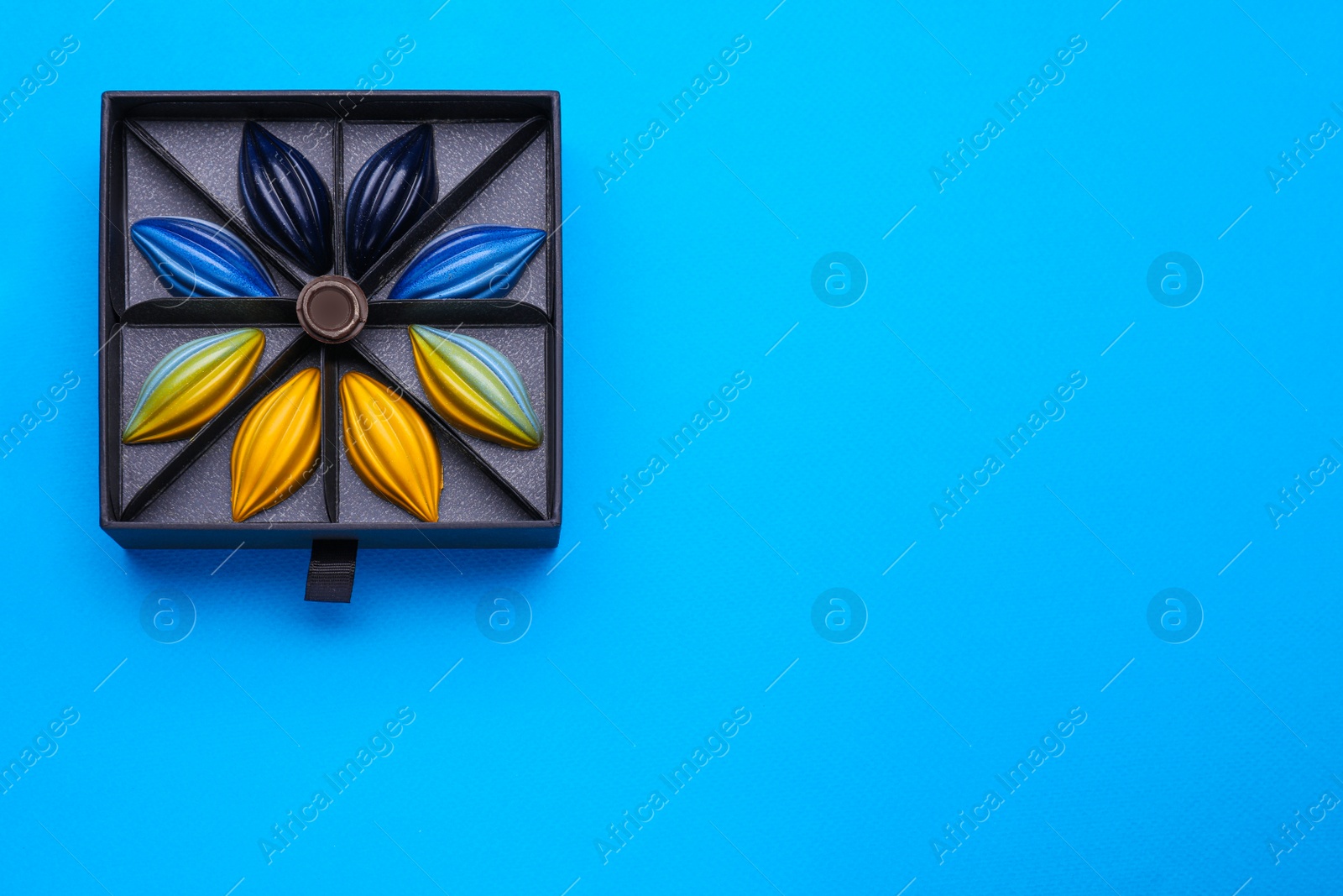 Photo of Box of tasty chocolate candies on blue background, top view. Space for text