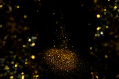 Photo of Sprinkling gold glitter on black background, bokeh effect