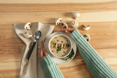 Photo of Woman with fresh mushroom soup at wooden table, top view