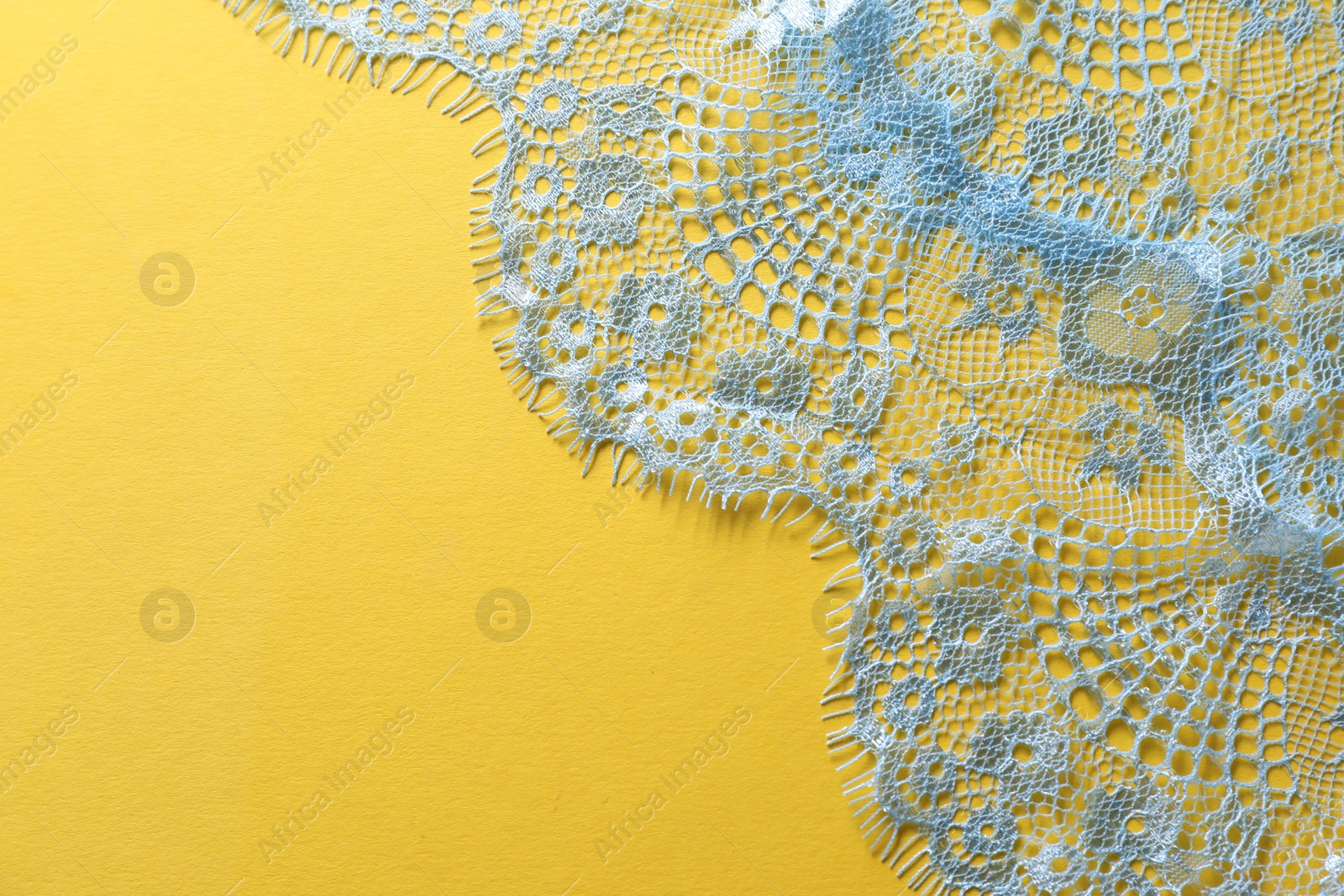 Photo of Light blue lace on yellow background, top view. Space for text