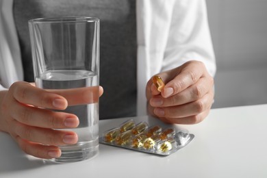 Woman with glass of water and pill at white table, closeup