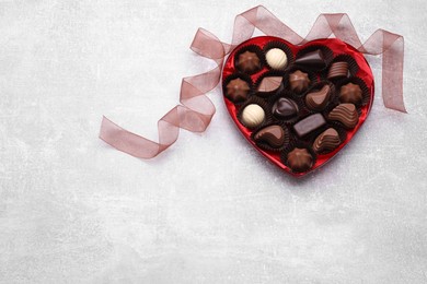 Heart shaped box with delicious chocolate candies and ribbon on light grey table, flat lay. Space for text