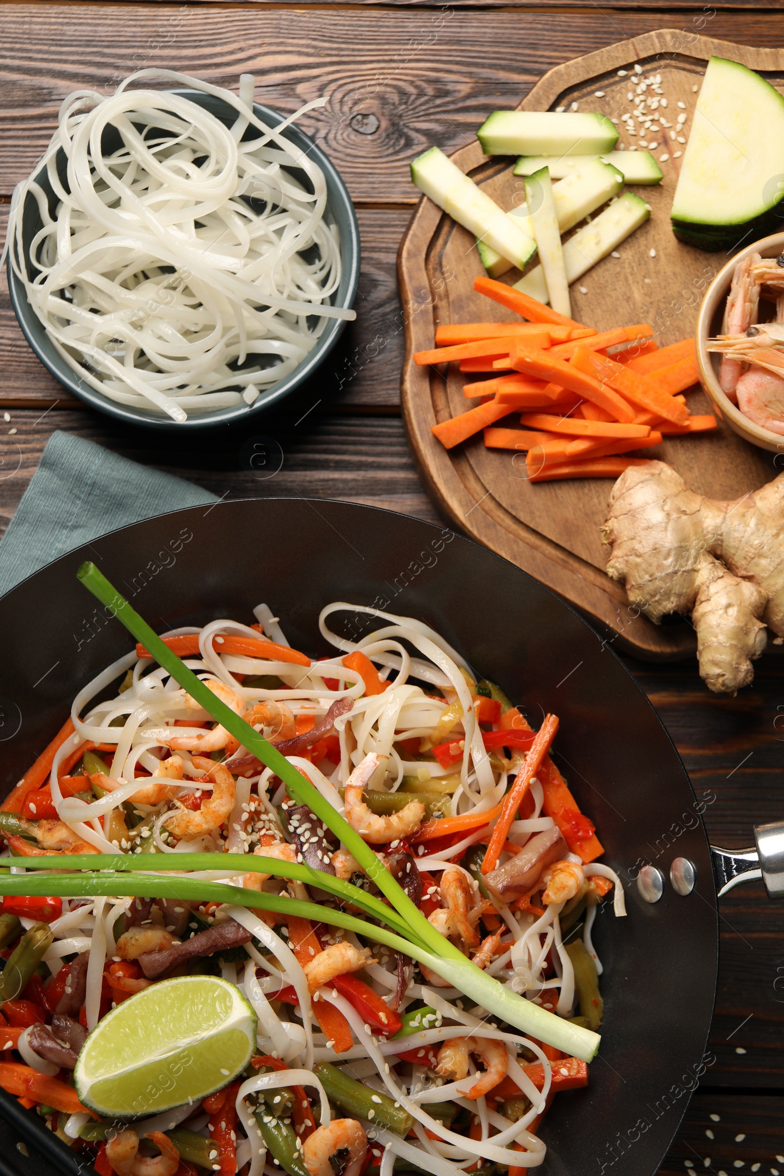 Photo of Shrimp stir fry with noodles and vegetables in wok on wooden table, flat lay