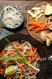 Shrimp stir fry with noodles and vegetables in wok on wooden table, flat lay