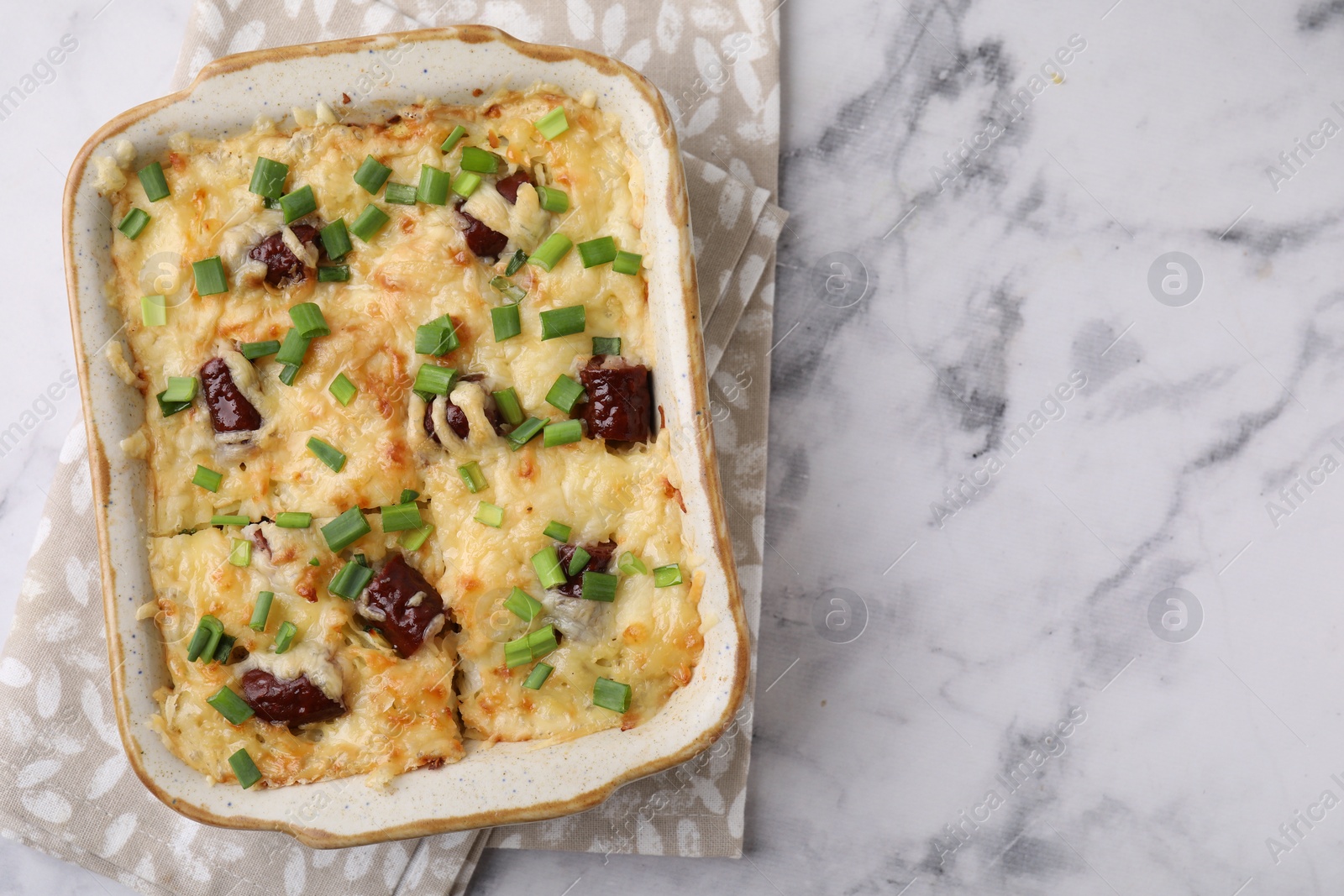 Photo of Tasty sausage casserole in baking dish on white marble table, top view. Space for text