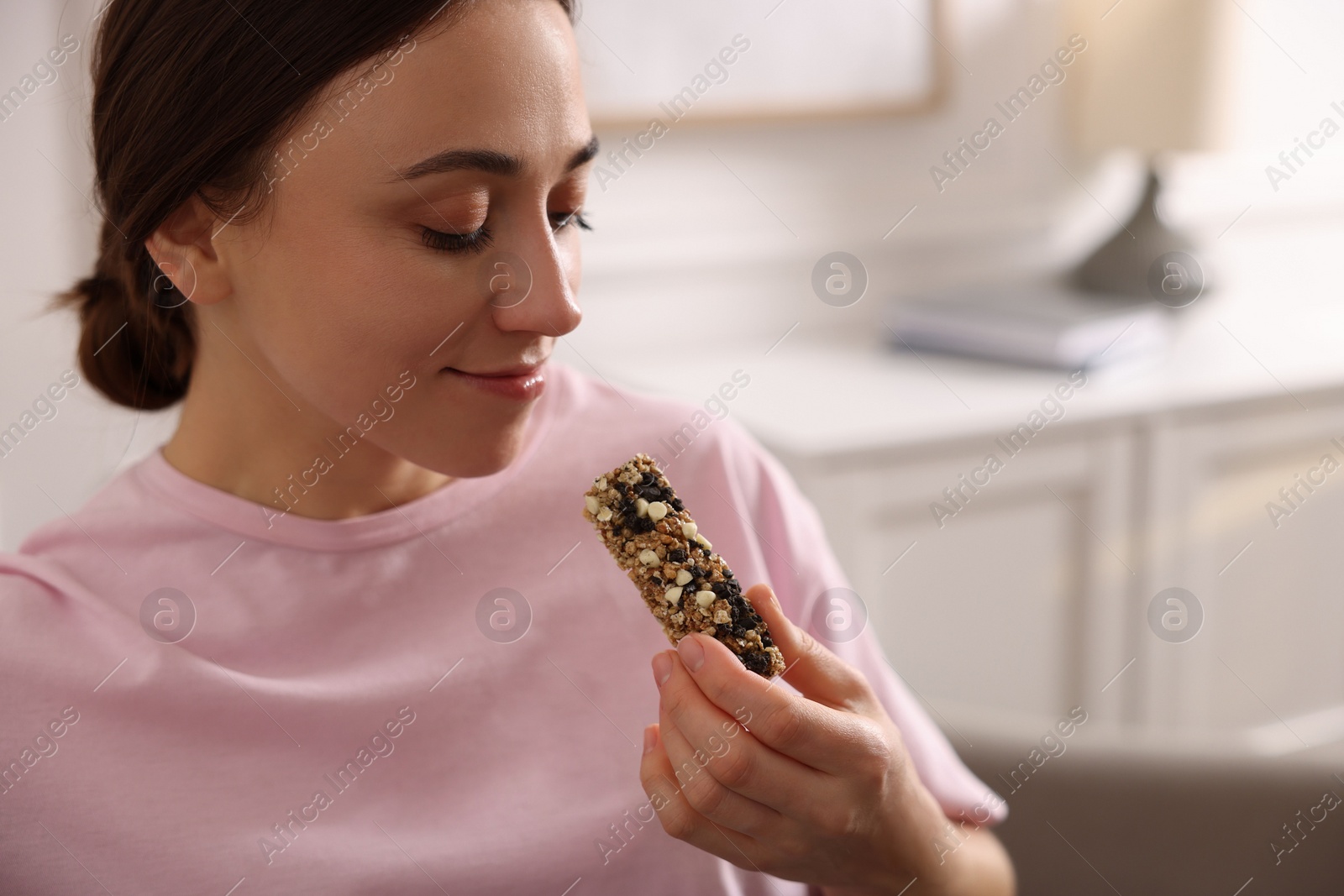 Photo of Woman eating tasty granola bar at home