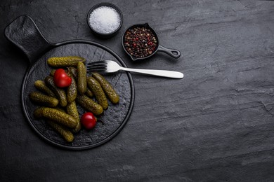 Photo of Serving board with pickled cucumbers and peppers on black table, flat lay. Space for text