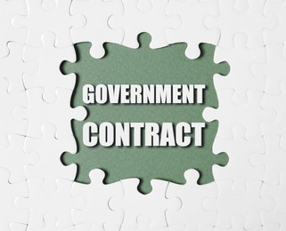 Image of Words Government Contract surrounded by white puzzle pieces on olive color background, top view
