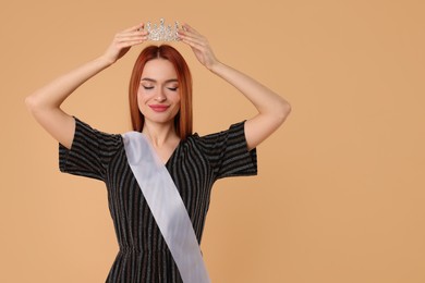 Photo of Beautiful young woman with tiara and ribbon in dress on beige background, space for text. Beauty contest