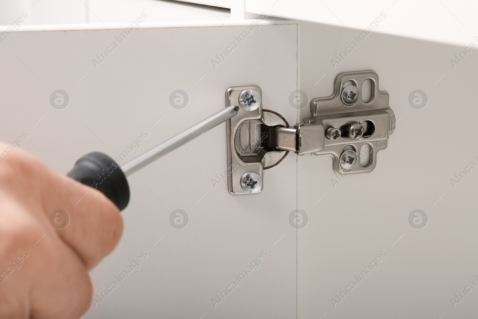 Photo of Man fixing door of white wardrobe with screwdriver, closeup