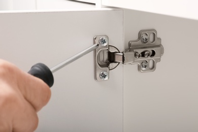 Photo of Man fixing door of white wardrobe with screwdriver, closeup