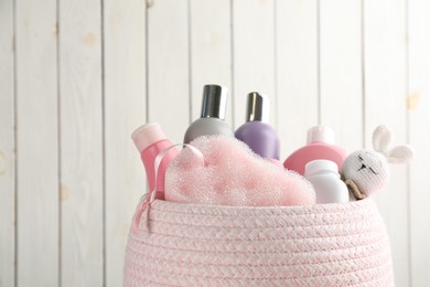 Photo of Basket full of different baby cosmetic products, bath sponge and toy on white wooden background
