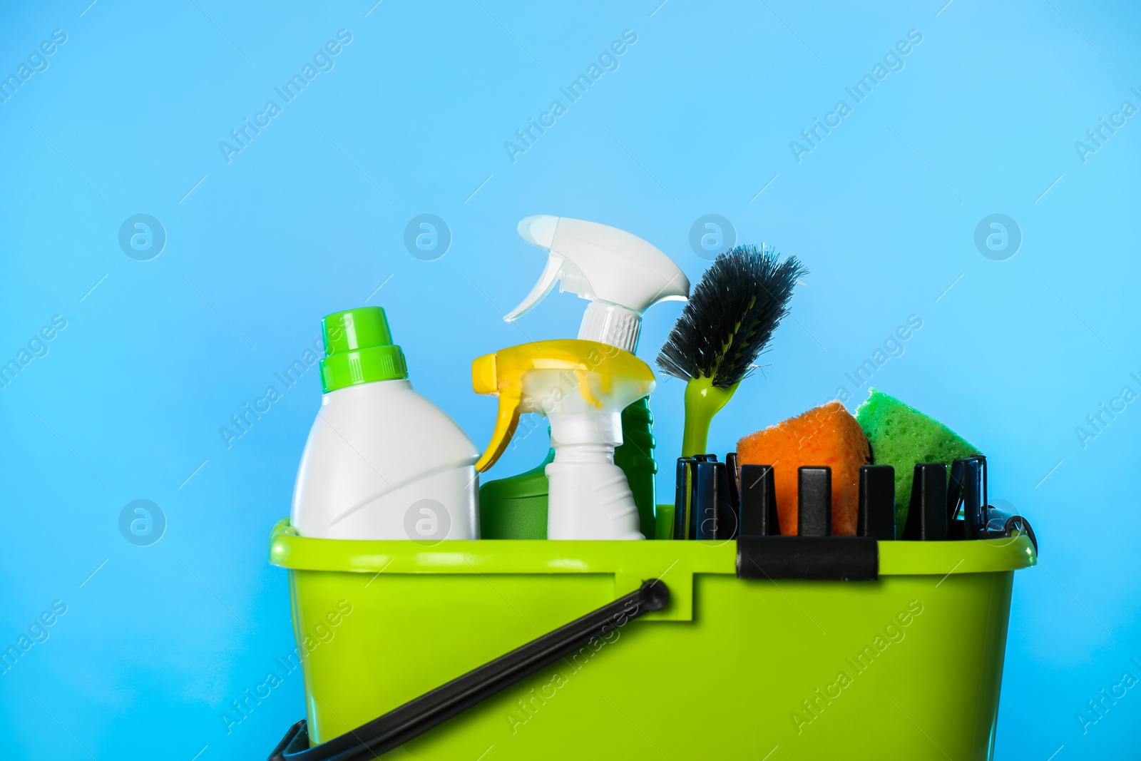 Photo of Bucket with different cleaning products and supplies on light blue background, closeup