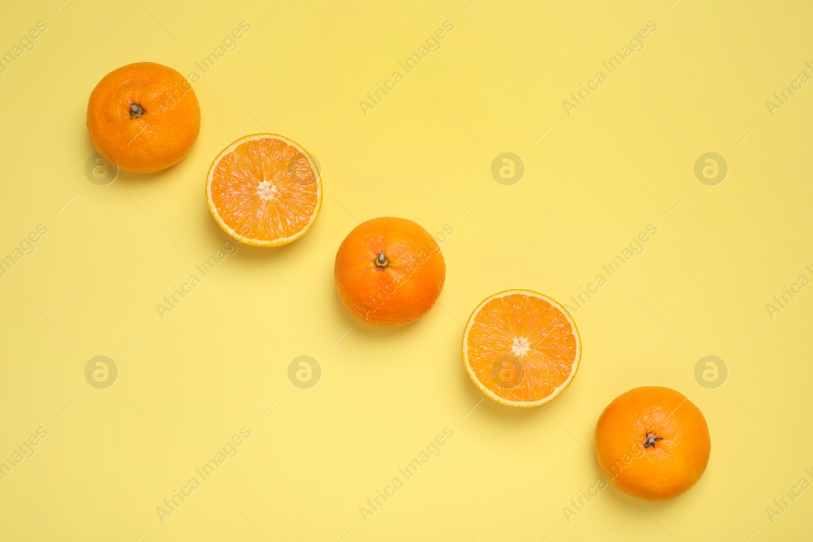 Photo of Cut and whole oranges on yellow background, flat lay
