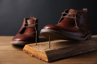 Photo of Metal nails in wooden plank and shoes on table