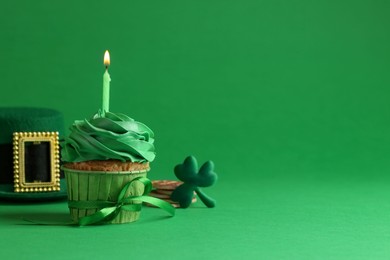 St. Patrick's day party. Tasty cupcake with burning candle and leprechaun hat on green background. Space for text