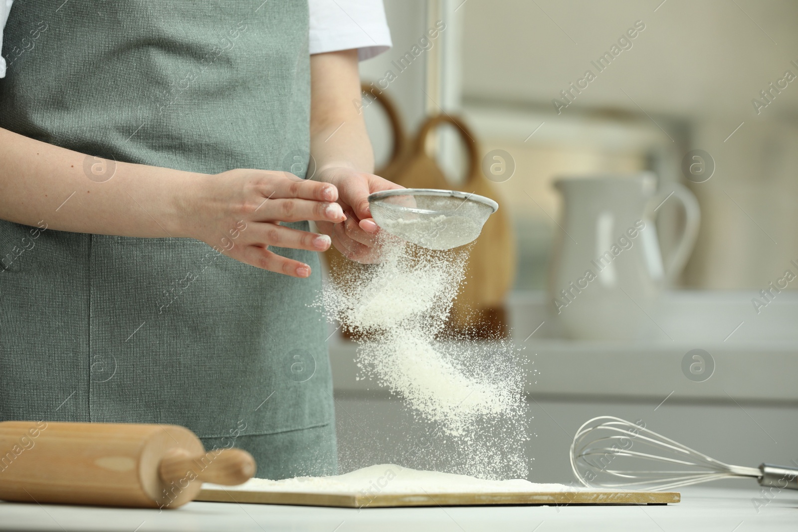 Photo of Woman sieving flour at table in kitchen, closeup. Space for text