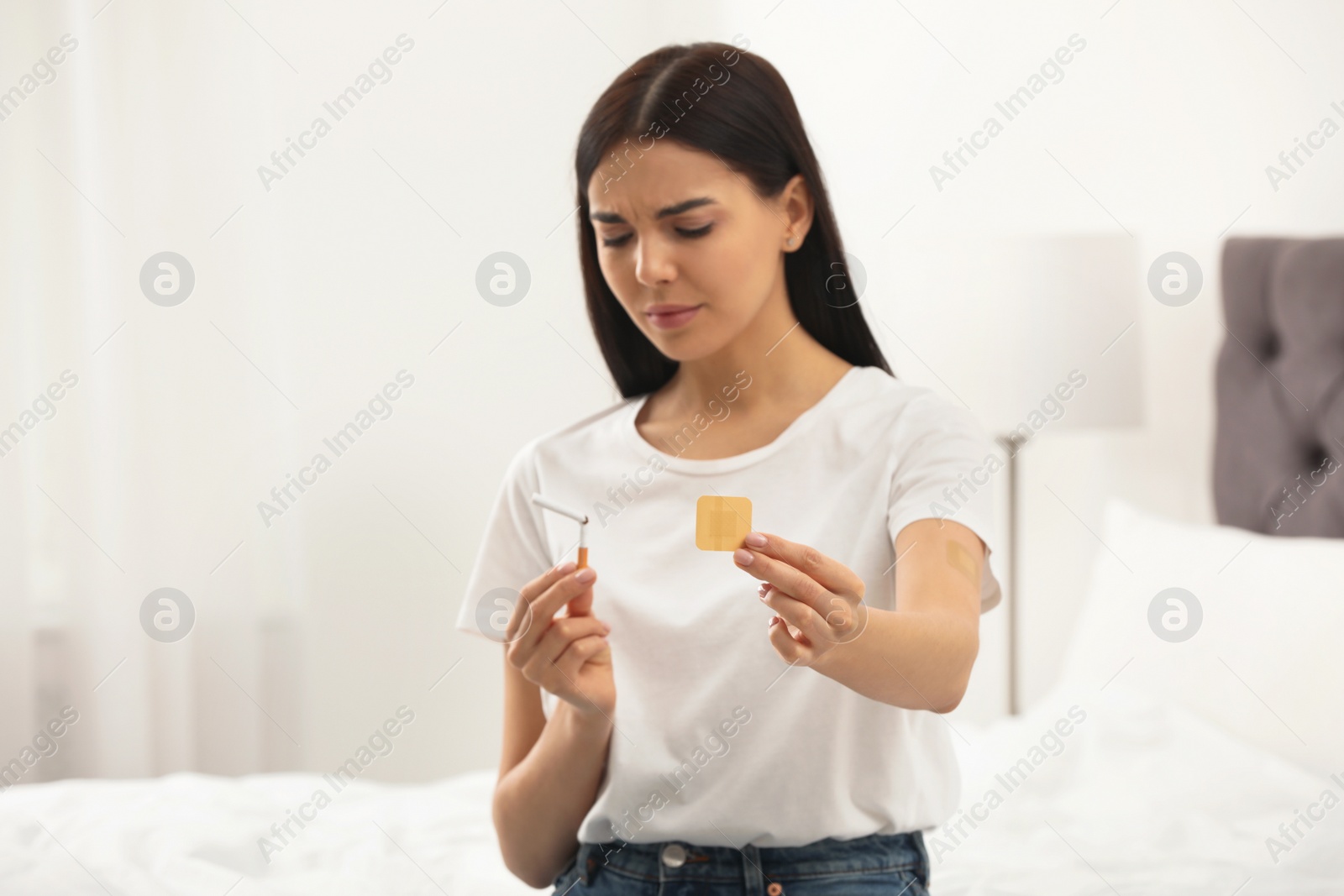 Photo of Emotional young woman with nicotine patch and cigarette in bedroom