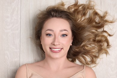 Portrait of smiling woman with curly hair on wooden floor, top view