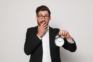 Photo of Emotional bearded man with alarm clock on light grey background. Being late concept