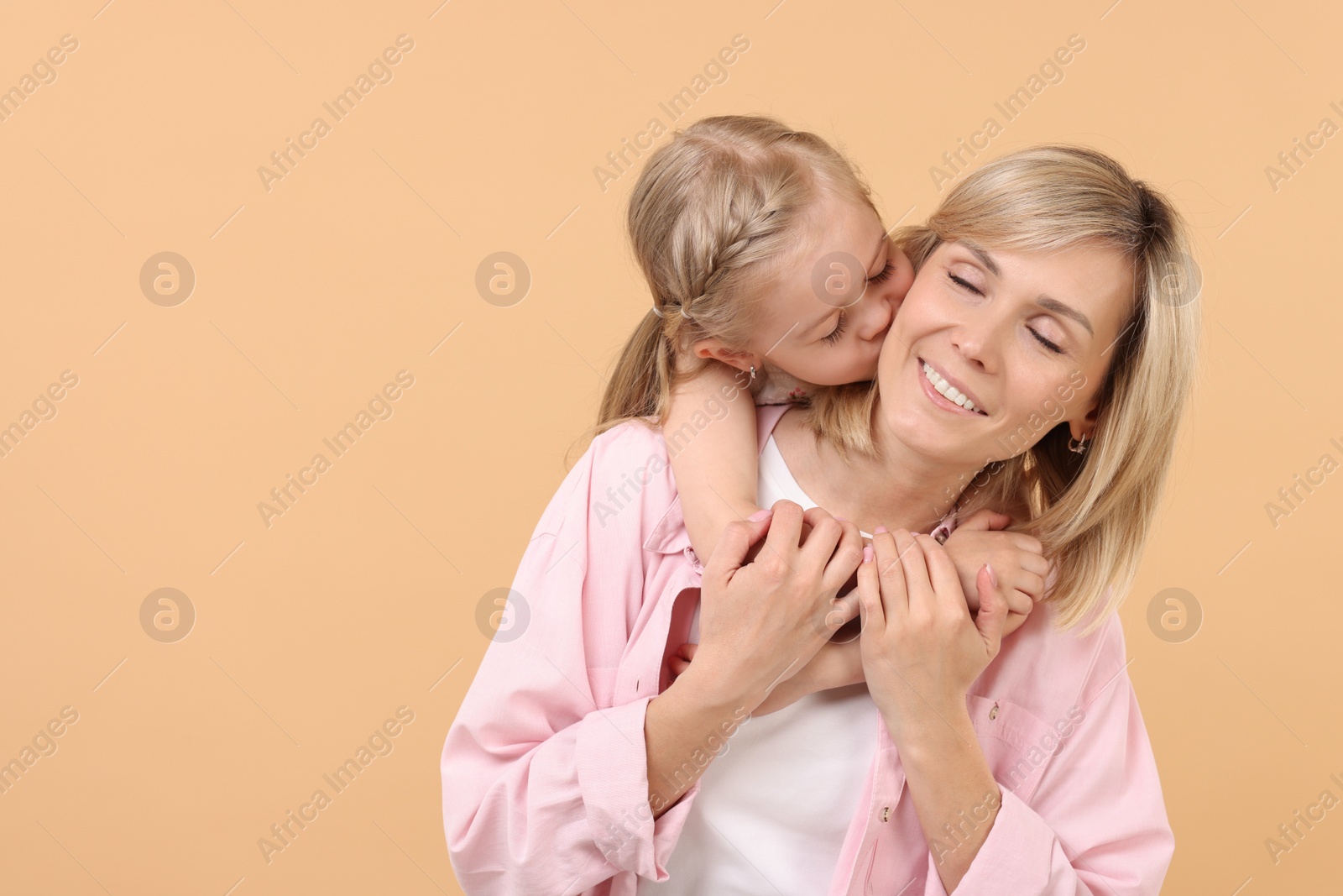 Photo of Daughter hugging and kissing her happy mother on beige background. Space for text