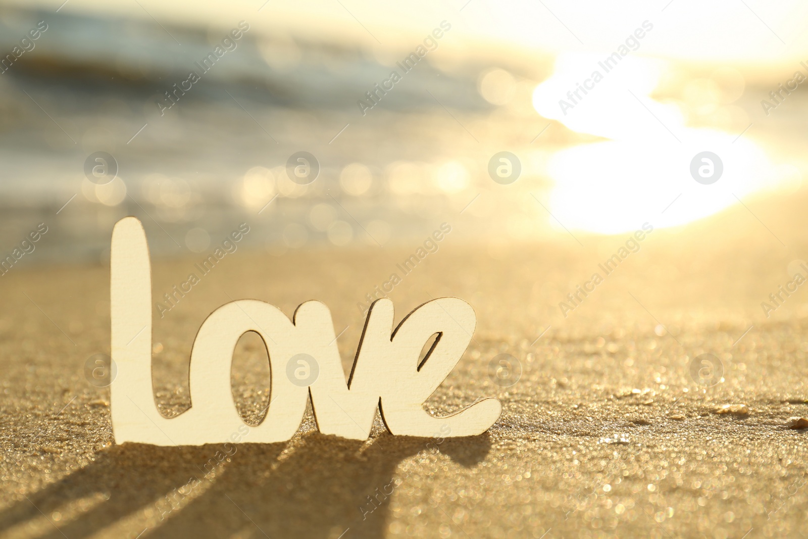 Photo of Word Love on sandy beach at sunset, closeup. Wedding concept