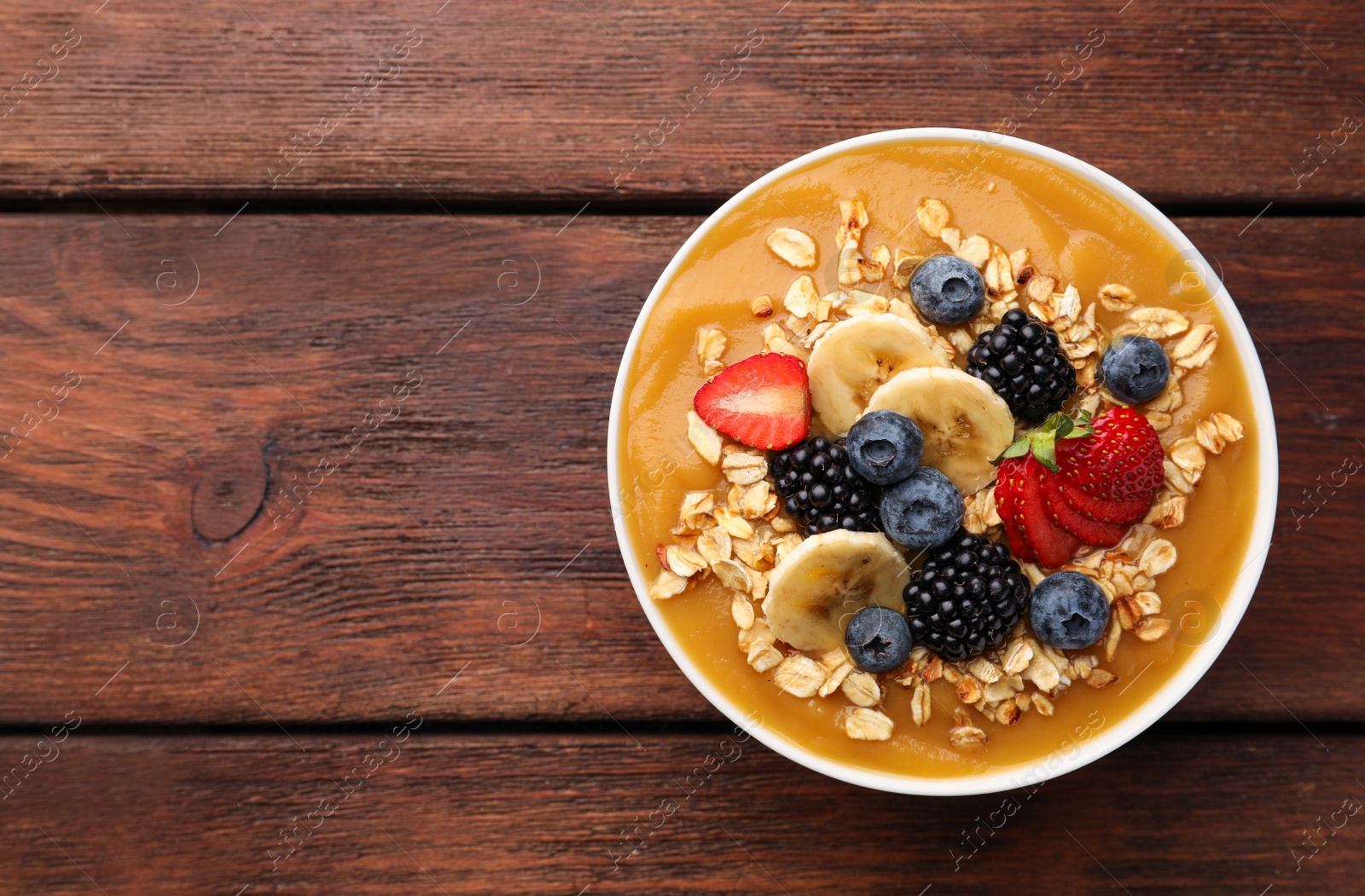 Photo of Delicious smoothie bowl with fresh berries, banana and oatmeal on wooden table, top view. Space for text