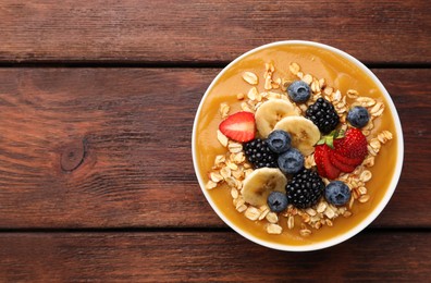 Photo of Delicious smoothie bowl with fresh berries, banana and oatmeal on wooden table, top view. Space for text