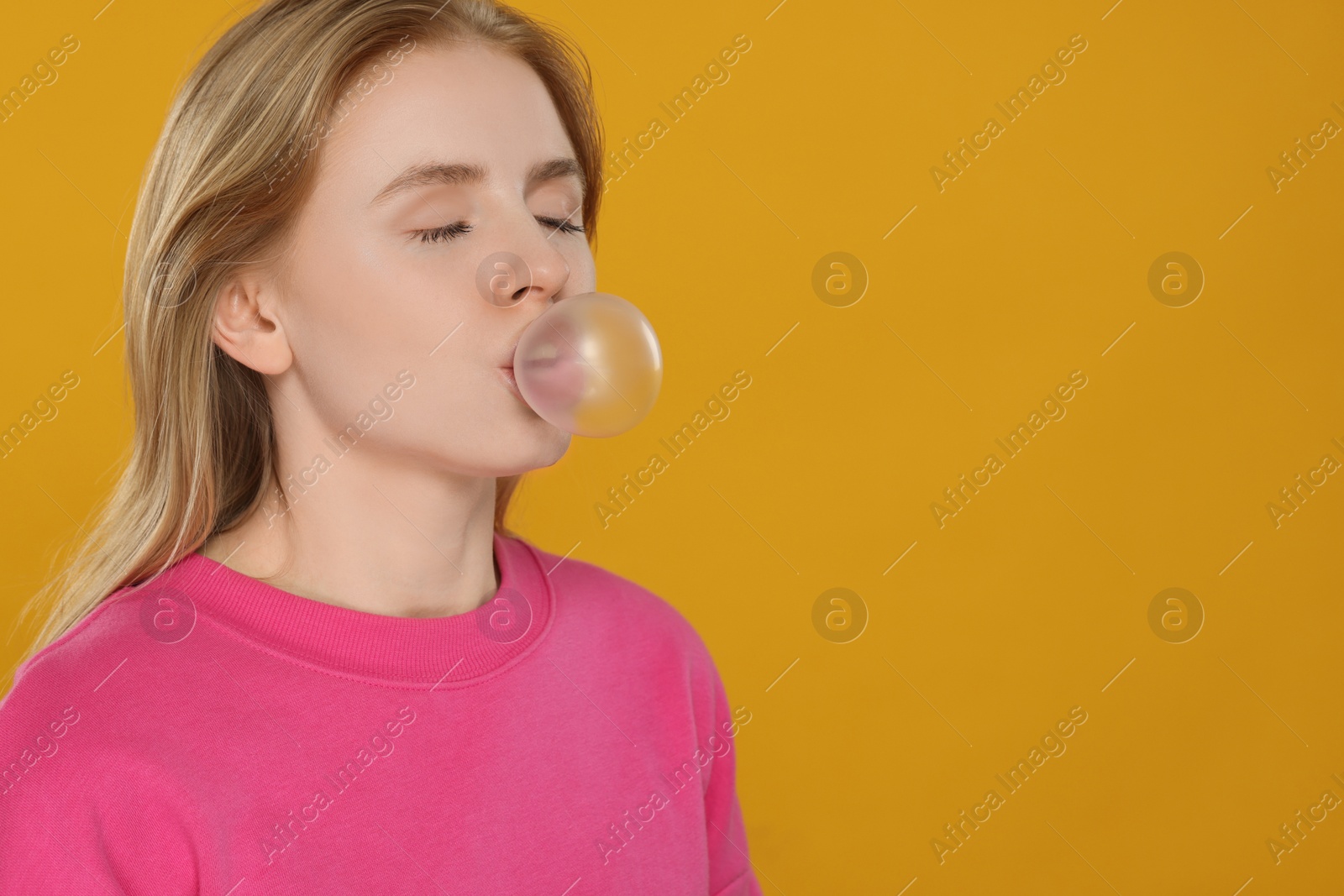 Photo of Beautiful young woman blowing bubble gum on yellow background. Space for text