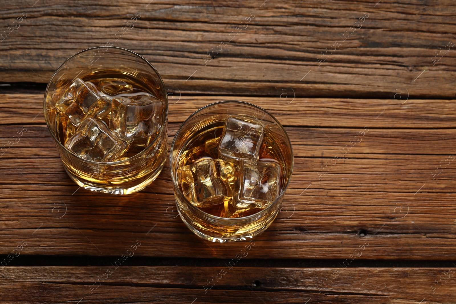 Photo of Whiskey with ice cubes in glasses on wooden table, above view. Space for text