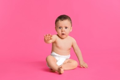 Photo of Cute baby in dry soft diaper sitting on pink background