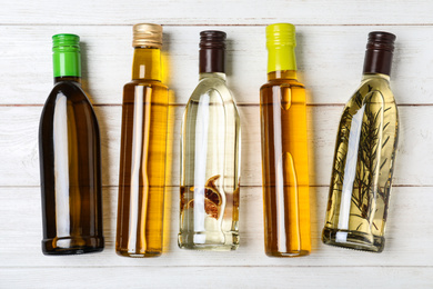 Photo of Different sorts of cooking oil in bottles on white wooden table, flat lay