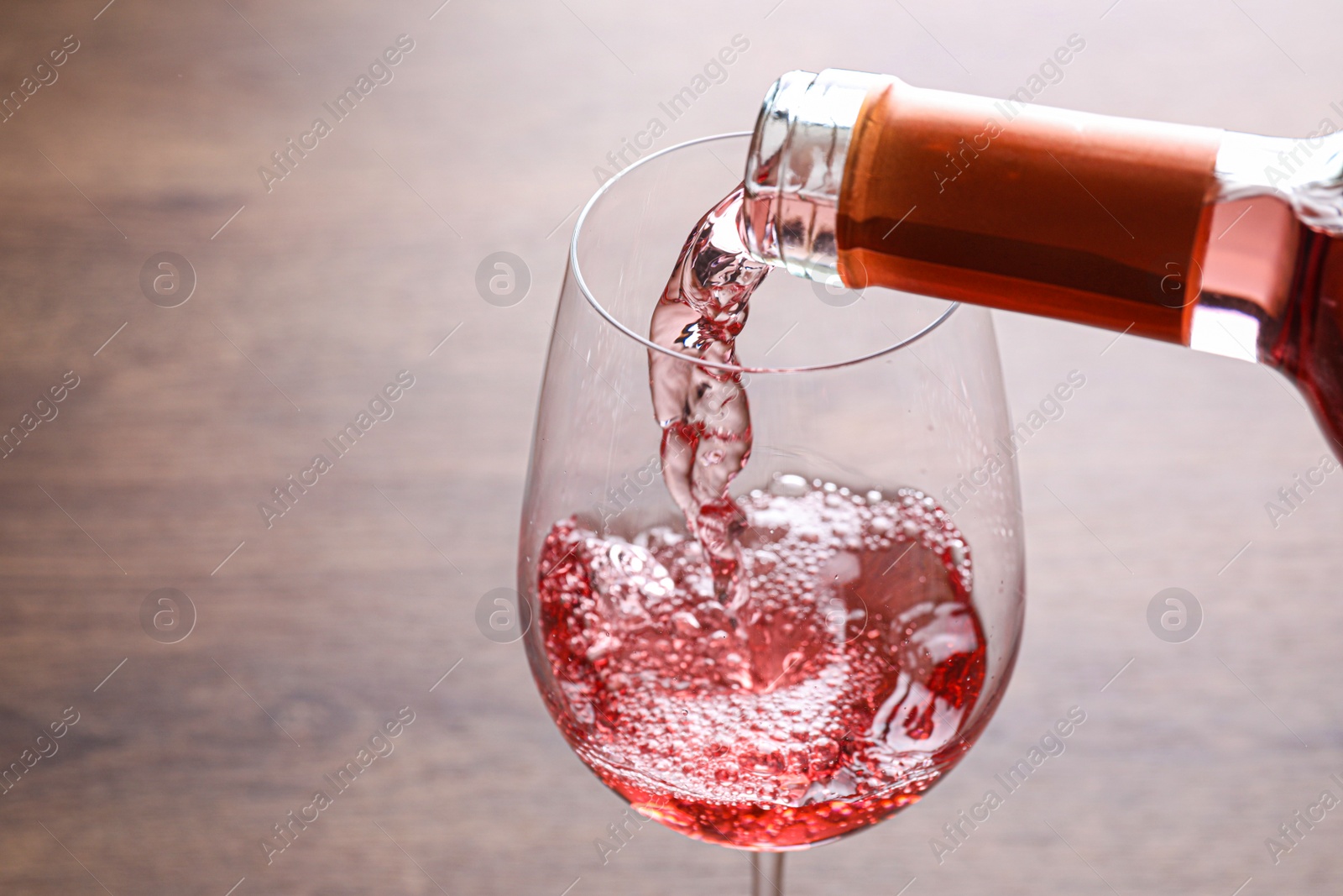 Photo of Pouring delicious rose wine into glass on wooden table, closeup