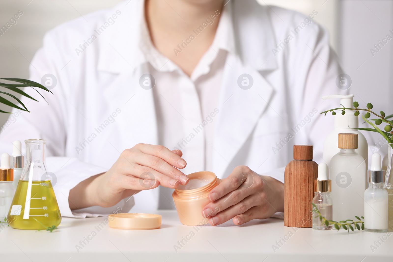 Photo of Dermatologist with jar testing cosmetic product at white table indoors, selective focus