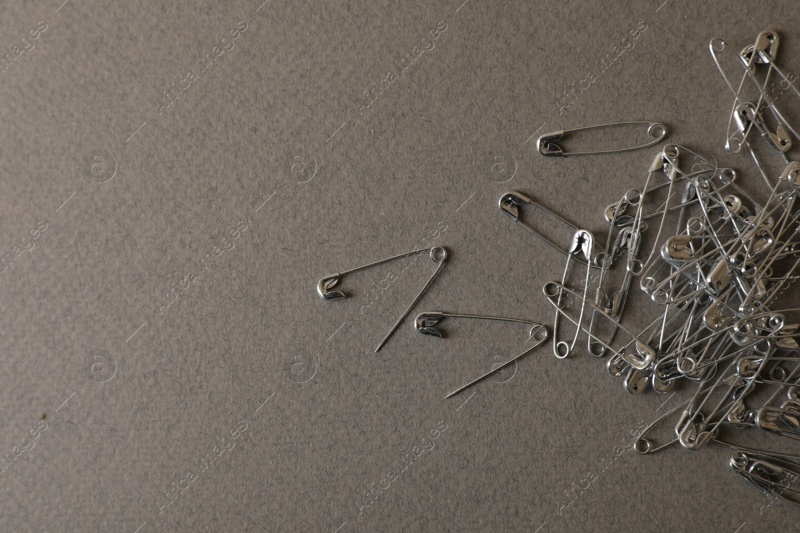 Photo of Pile of safety pins on grey textured background, flat lay. Space for text