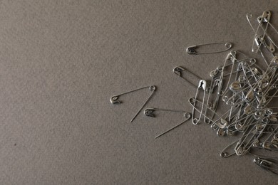 Photo of Pile of safety pins on grey textured background, flat lay. Space for text