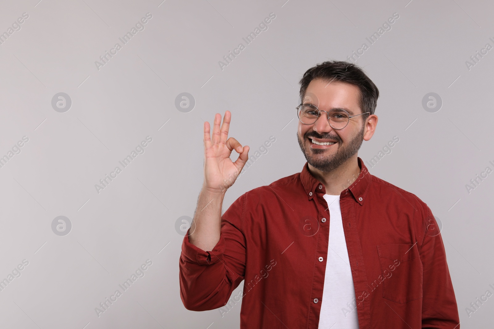 Photo of Portrait of happy man in stylish glasses showing OK gesture on light grey background, space for text