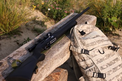 Photo of Hunting rifle and backpack on wooden bench outdoors