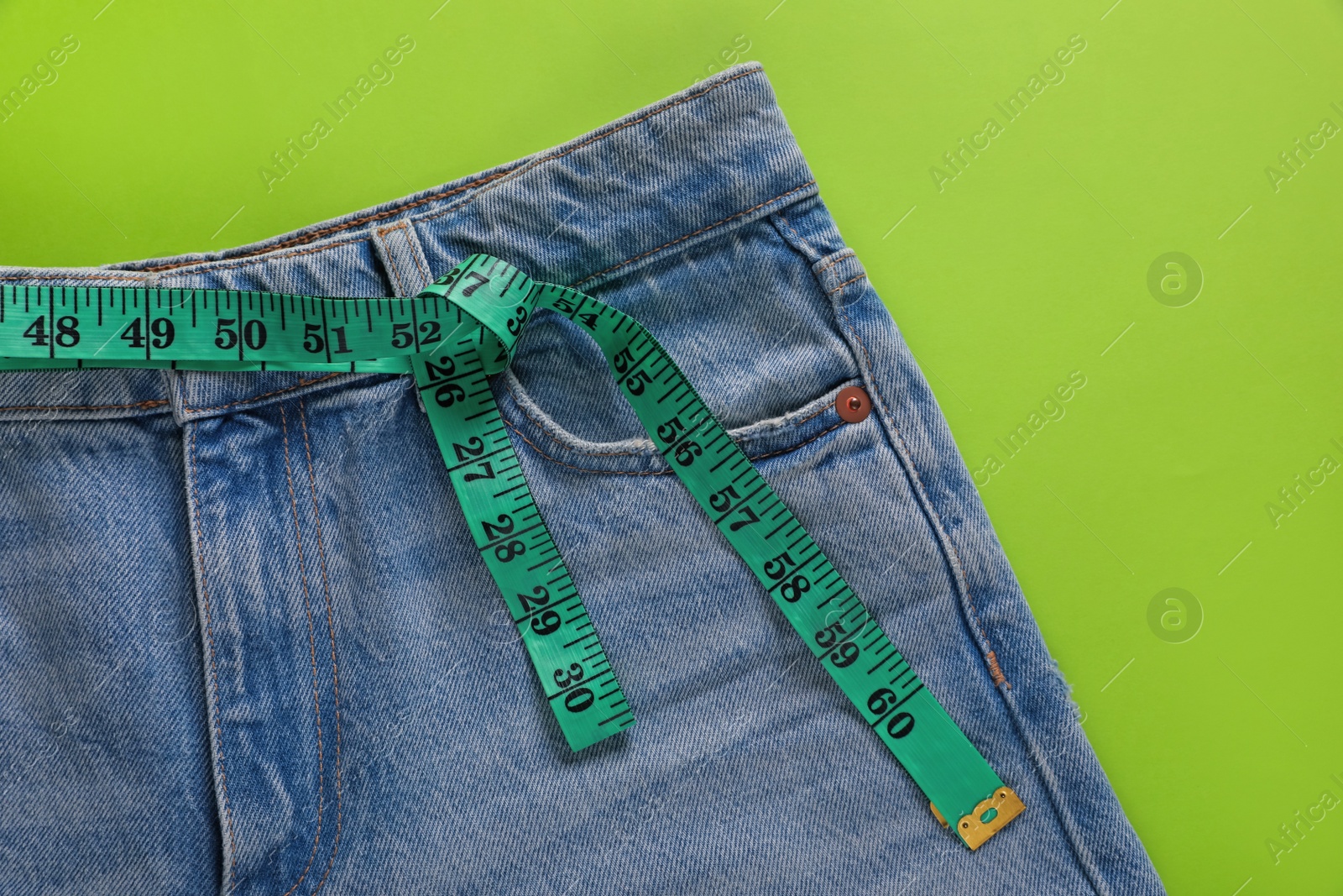 Photo of Jeans and measuring tape on light green background, top view. Weight loss concept