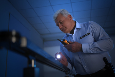 Professional security guard with portable radio set and flashlight in dark room