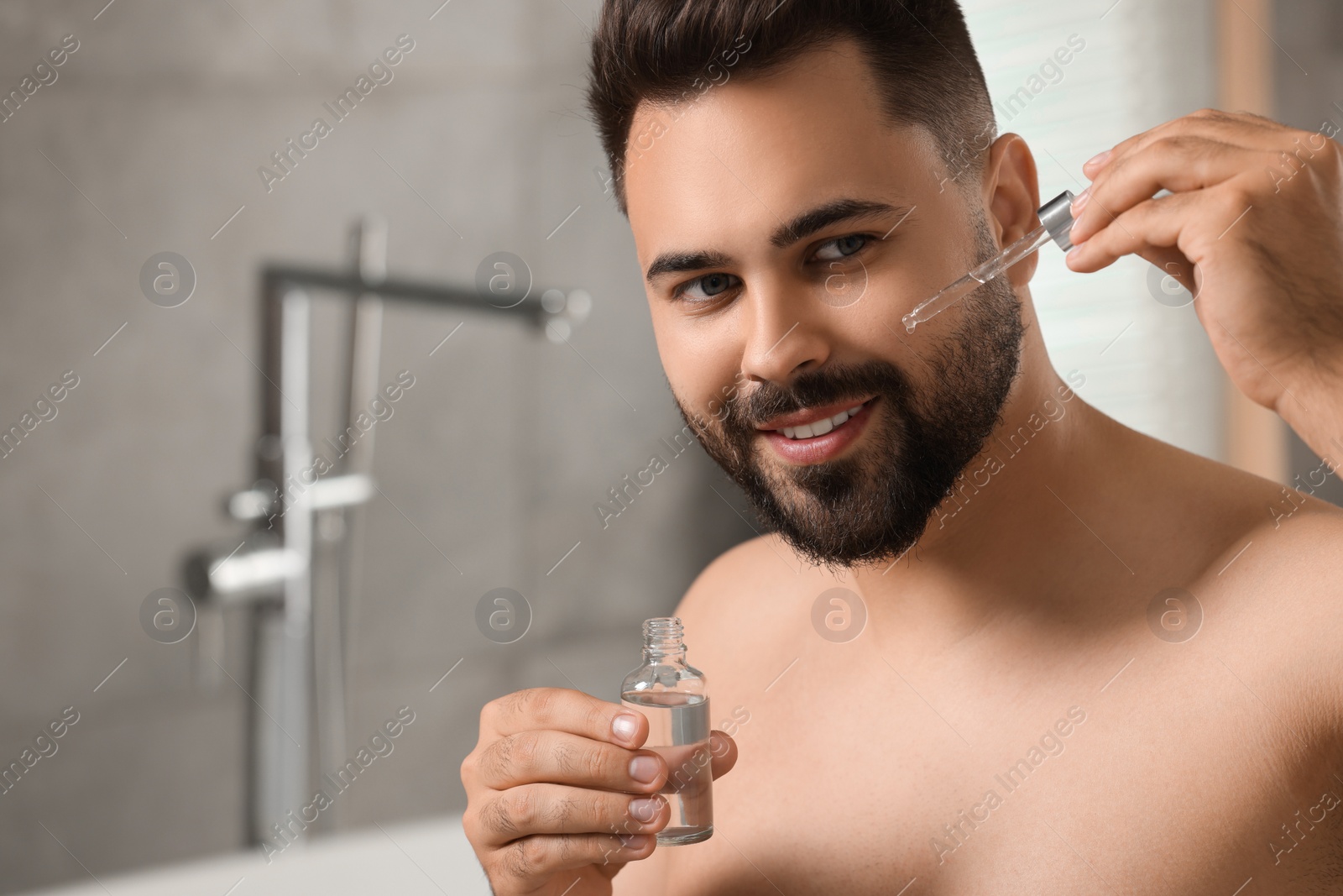 Photo of Handsome man applying cosmetic serum onto his face in bathroom. Space for text