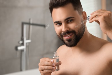 Handsome man applying cosmetic serum onto his face in bathroom. Space for text