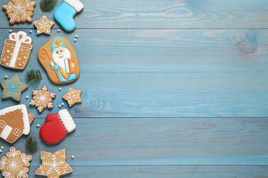 Tasty gingerbread cookies and fir branches on light blue wooden table, flat lay with space for text. St. Nicholas Day celebration