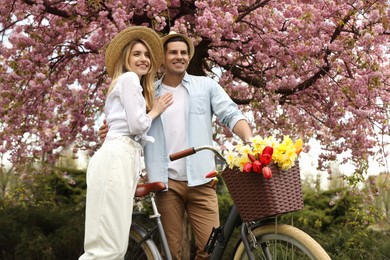 Lovely couple with bicycle and flowers in park on pleasant spring day